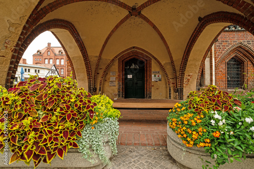 Historic Gothic brick arcade with pointed arches, vaulted ceiling and colorful flower planters at the old town hall, photographed in landscape format