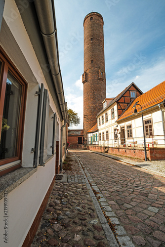 Full view of the historic Schrotturm rising above a narrow cobblestone street and traditional old town buildings, photographed in portrait format.