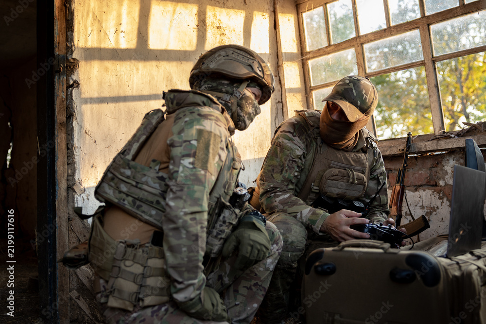 Obraz premium Soldiers operate a drone control console. Military personnel are carrying out a combat mission at a position in an abandoned house.
