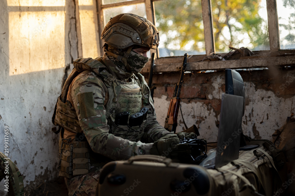 Obraz premium Soldier operates a drone control console. Military personnel is carrying out a combat mission at a position in an abandoned house.