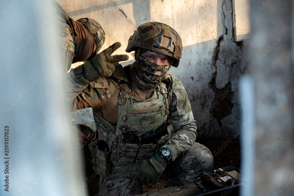 Obraz premium Soldier operates a drone control console. Military personnel is carrying out a combat mission at a position in an abandoned house.
