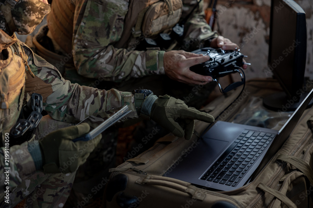 Obraz premium Soldiers operate a drone control console. Military personnel are carrying out a combat mission at a position in an abandoned house.