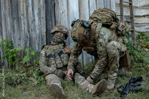 Military soldier applies a tourniquet to the leg of a wounded comrade. Combat tactical equipment. Combat use Turnstile.