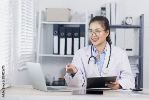 Asian female doctor having an online consultation with a patient via laptop in her office, holding an X-ray scan report.