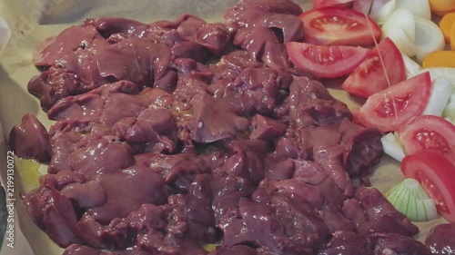 Raw chicken liver being prepared on a baking sheet with fresh chopped vegetables. A healthy and delicious homemade meal preparation concept