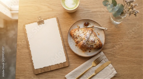 Clipboard with blank paper beside croissant and matcha latte