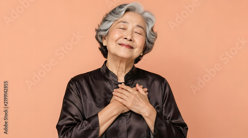 Happy elderly Asian woman with closed eyes and hands over heart.