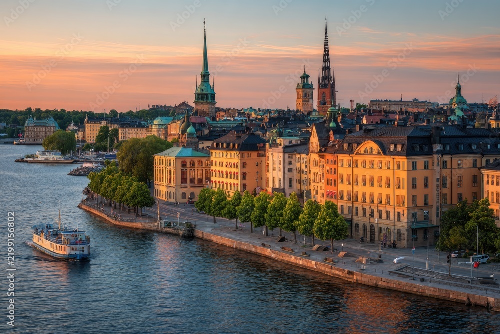 Obraz premium Scenic waterside cityscape featuring historic architecture, boat, and a stunning sunset