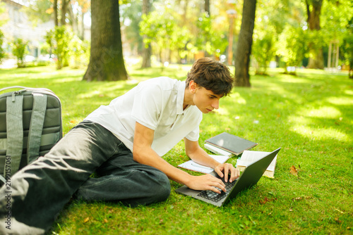 Canvas Print Dedicated dark-haired scholar working on a computer on the campus lawn