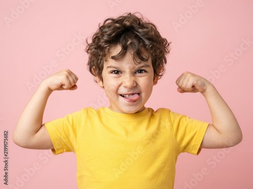 Funny little sportive kid boy in yellow shirt, showing his muscles. Happy strong nerd kindergarten child showing bicep. Dream, confidence, success, possible, innovation. Go back elementary school.
