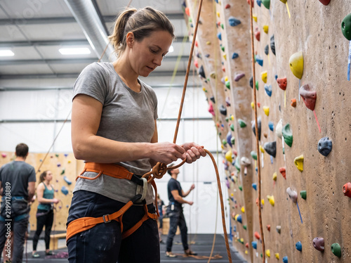 Young woman preparing climbing gear in indoor rock climbing gym  