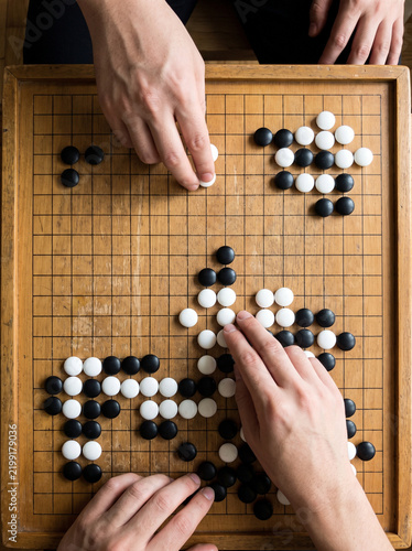 Two hands playing a game of Go on a wooden board  