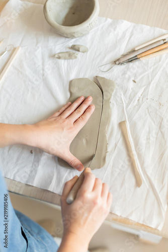 Women artist pottery shaping clay on a worktable with tools and cloth in a top-down perspective, focused and creative activity in crafting and production of handmade ceramics