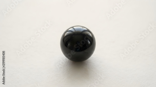 A perfectly spherical black marble resting on a neutral surface, reflecting light.