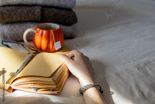 Картината върху платно Hand rests on open journal page with pumpkin mug and sweaters visible in background