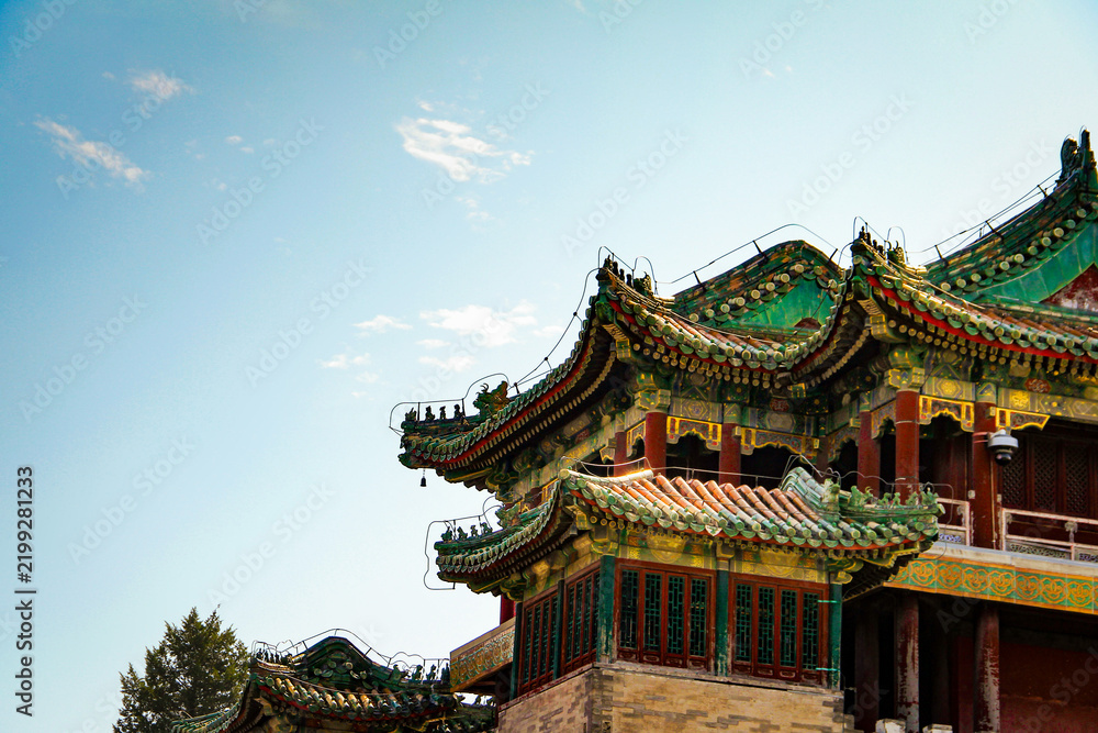 Fototapeta premium Detailed view of a traditional Chinese temple featuring green glazed tile roofs and ornate red wooden architecture under a clear blue sky.