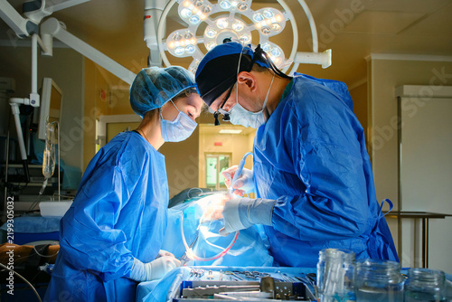 Surgeon and assistant performing surgery under operating room lights