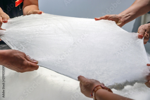 Obraz na płótnie Multiple hands pull and stretch a fragile white sheet of raw silk in a hands-on