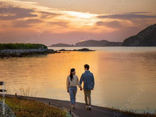 カップルが夕日を眺めて海岸を歩く