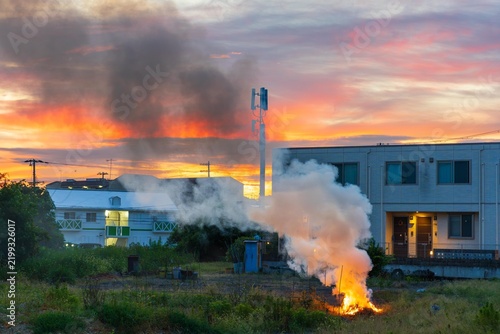 Open flame and smoke cloud by apartment building and antenna tower at sunrise