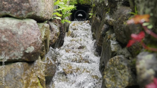 Water flows from pipe down rock canal with green and red leaves