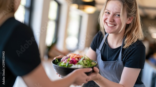 Smiling young woman serving poke bowl in apron, casual food service, healthy meal prep, restaurant menu and poke bowl catering use case