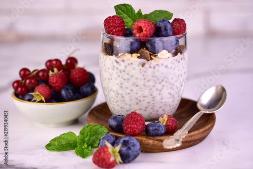 A glass of chia seed pudding with fresh berries on a white background.
