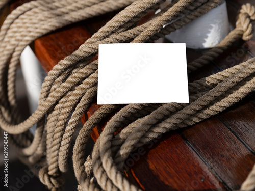A blank white card sits straight on coiled rope against varnished wood, a clean nautical still life for invitations or branding.