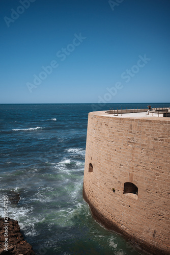Fotografie Fort near the ocean with waves crashing against its base on a sunny day
