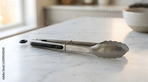 A single stainless steel kitchen accessories tool for cooking resting on a bright white marble countertop in a kitchen