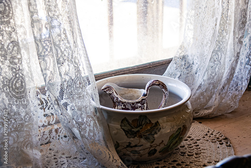 Vintage ceramic water pitcher and basin by lacy window curtains