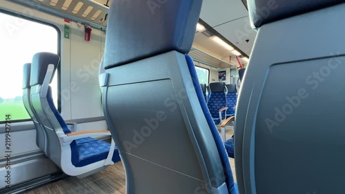 Interior view of a modern passenger train carriage with comfortable blue seats, large windows, and bright ceiling lighting.