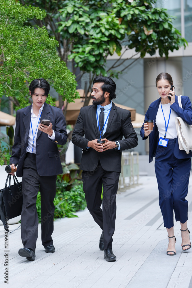 Fototapeta premium A multiethnic business team of three colleagues commute on foot while handling calls and messages beside the polished facade of a new mixed use city (frame 173)