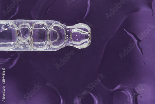 Glass Pipette Positioned Horizontally With Visible Air Bubbles And Droplets Over Textured Purple Surface Close-Up Studio Setting For Cosmetic Or Laboratory Product Detail Imagery.