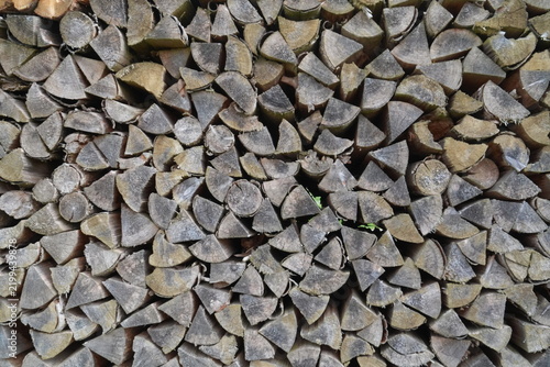 Tightly stacked split logs fill the frame, showing varied cut ends, bark, grain, cracks and natural brown and gray wood tones
