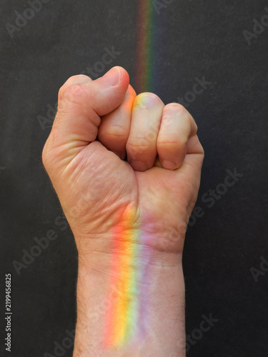 Rainbow reflection on hand, raised fist of a man for PRIDE month, the LGBTQIA+ movement. Pride day for sexuality freedom, love diversity celebration. Close up of a man fist with lgbt