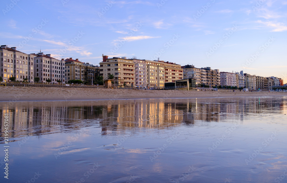 Obraz premium Sunset over Zurriola beach with city reflection on wet sand, San Sebastian, Basque Country, Spain