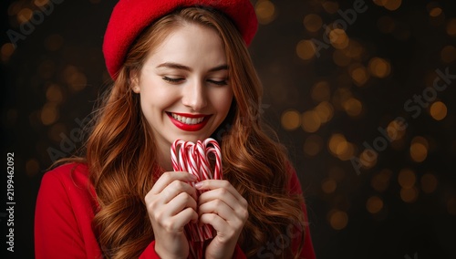 Woman Holds Candy Canes While Smiling in a Cozy Setting With Warm Lights Duri...