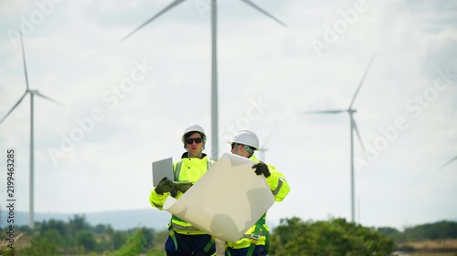 Engineers wearing safety helmets and jackets inspecting a wind turbine at wind farm at sunset. Concept renewable energy, sustainable technology wind power maintenance and environmental engineering.