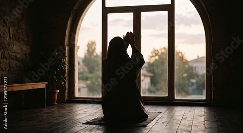 Silent Prayer by the Window: Silhouetted figure in prayer, hands raised in devotion, facing a large arched window with the soft light of dusk filtering through.