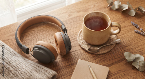 Relaxing Break with Tea and Headphones: A cozy scene featuring a warm cup of tea, a pair of stylish headphones, and a notebook on a wooden table, perfect for a moment of relaxation and inspiration.