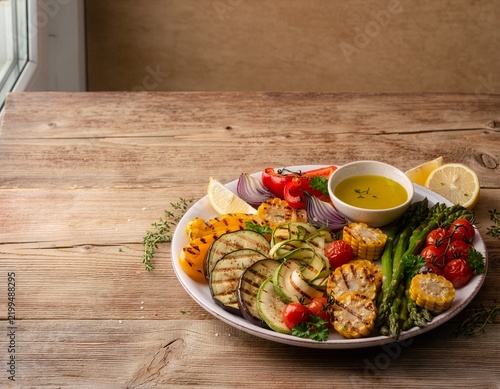 Grilled fresh vegetables platter with zucchini, corn, asparagus, red bell pepper, cherry tomatoes, purple onion and lemon wedges served with herb sauce
