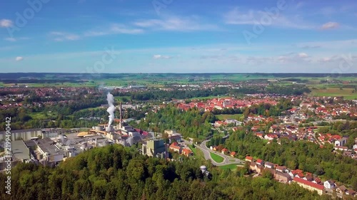 Aerial drone video of Schongau, Bavaria, Germany, showing residential neighborhoods, an industrial area, surrounding forests and rolling countryside under a blue sky