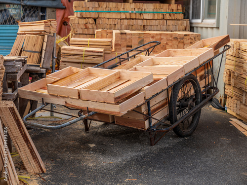 View of a wooden handcart loaded with empty wooden crates in a lumber yard with stacks of timber planks in the background, Busan, Busan, South Korea.