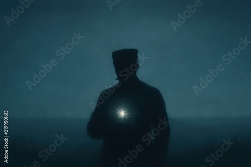 A mysterious silhouette of a person holding a bright light seems to illuminate the darkness and create a sense of wonder within the moody atmosphere