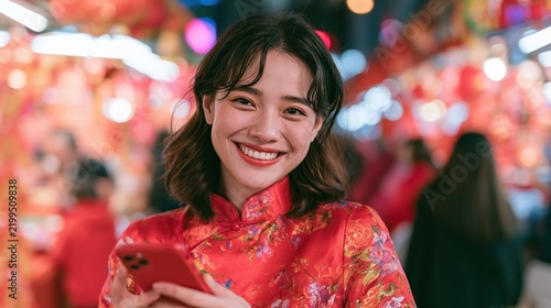 A young woman in a red traditional dress smiles while holding a phone amidst vibrant, festive lanterns glowing in the background.