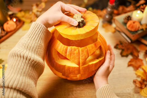 Woman hands placing lid on carved pumpkin for Halloween decorating and preparation, creating cozy craft for autumn holiday tradition and festive celebration.