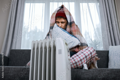 Quadro su tela Cold man freezing at home near electric heater during energy crisis, facing heating problem and rising costs in cold weather, shivering under blanket during winter frost and cold snap