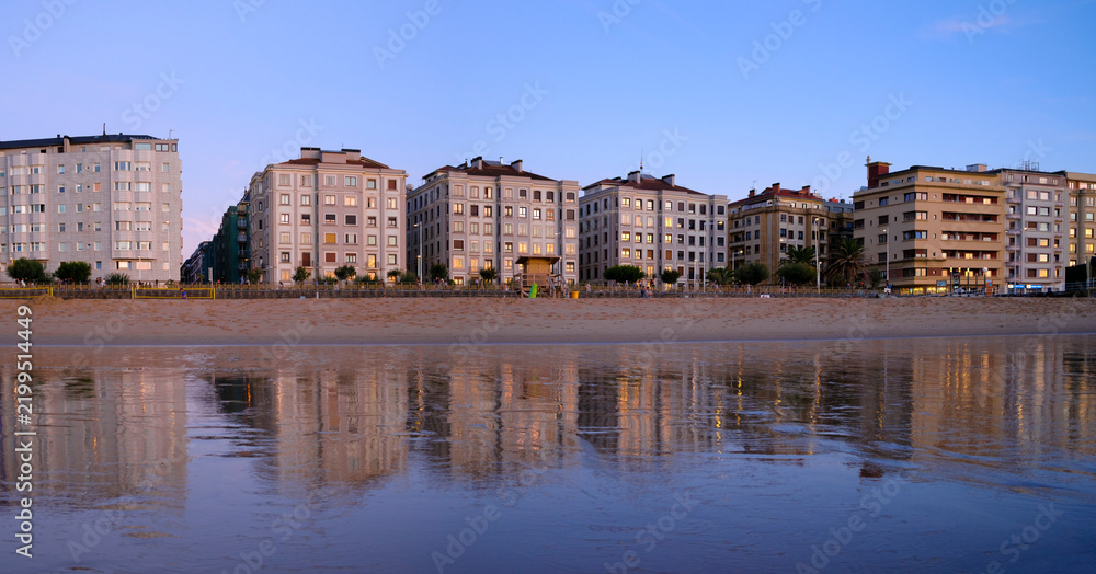 Obraz premium Sunset over Zurriola beach with city reflection on wet sand, San Sebastian, Basque Country, Spain