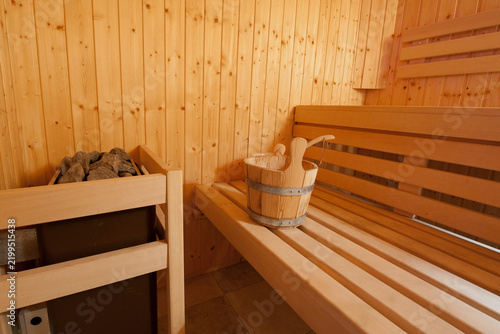 A wooden sauna interior featuring a bench, a bucket, and a container of rocks. The setting is warm and inviting, illuminated by soft lighting.